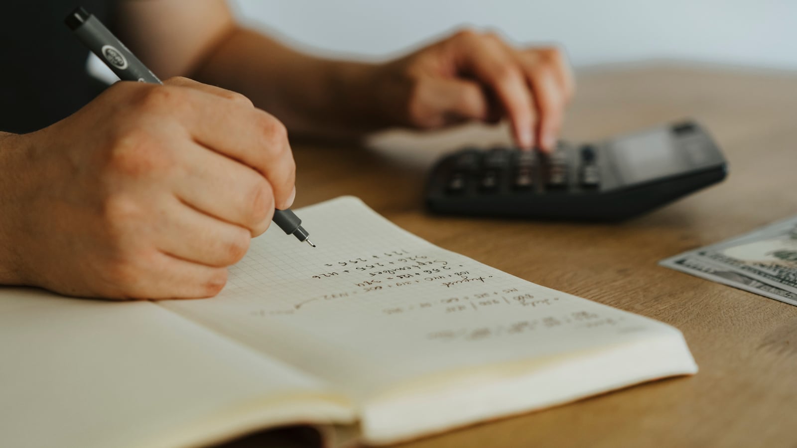 Una persona calcula un presupuesto con calculadora y cuaderno en la mesa.