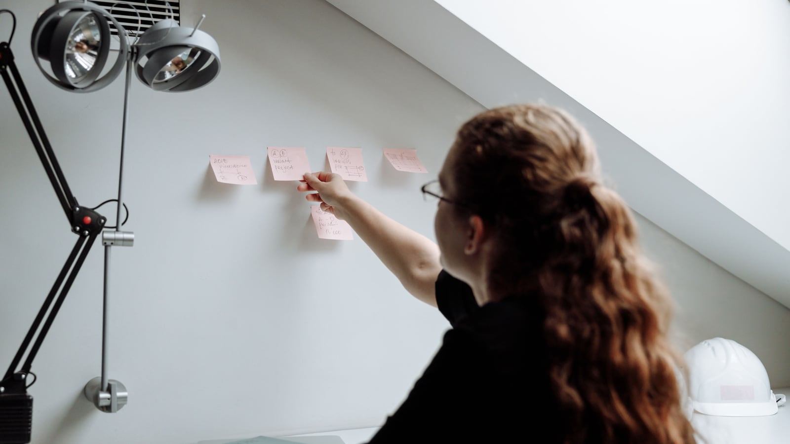 Una persona planifica los pasos de un proceso con notas adhesivas de colores en la pared de la oficina.