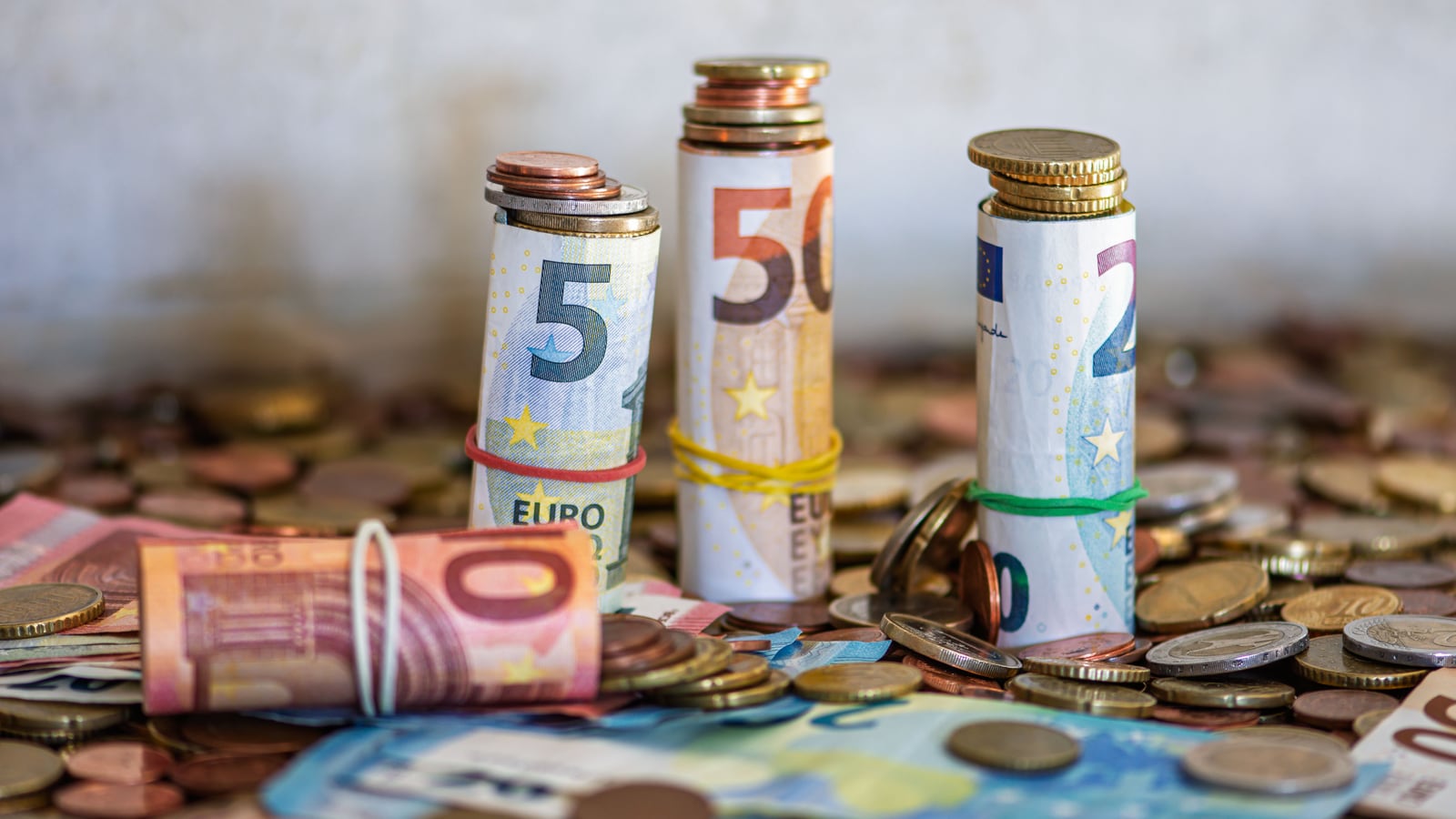 Una persona ahorra tiempo y dinero: monedas de euro apiladas junto a un reloj y una calculadora en el escritorio.